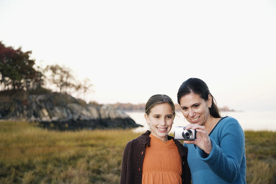 Mid adult woman and her daughter looking at a digital camera Photograph by Glow Images