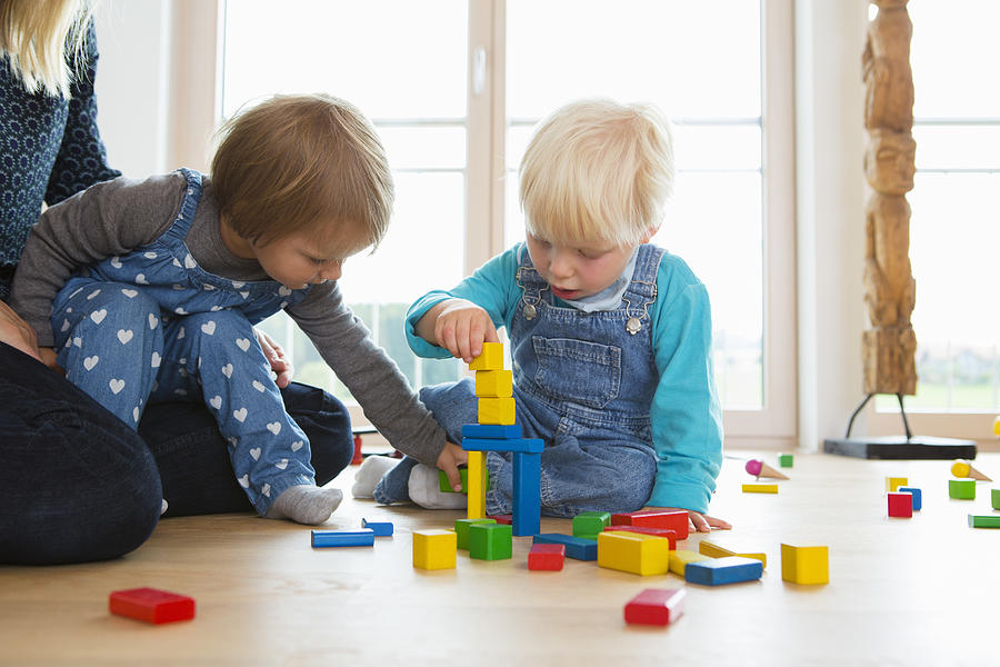 Mid adult woman and two toddlers playing with building bricks on living room floor Photograph by Judith Haeusler