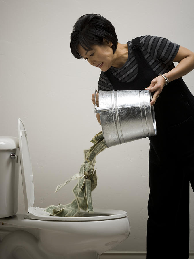 Mid adult woman emptying a bucket of money into a toilet bowl Photograph by Rubberball