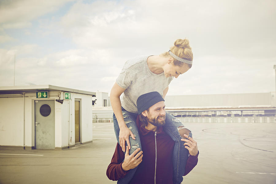 Mid adult woman getting shoulder ride from boyfriend on rooftop parking lot Photograph by Severin Schweiger