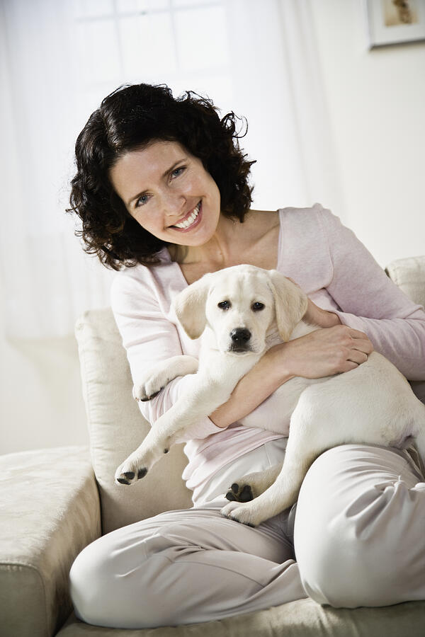 Mid adult woman sitting on sofa, holding puppy dog, smiling, portrait Photograph by Andersen Ross