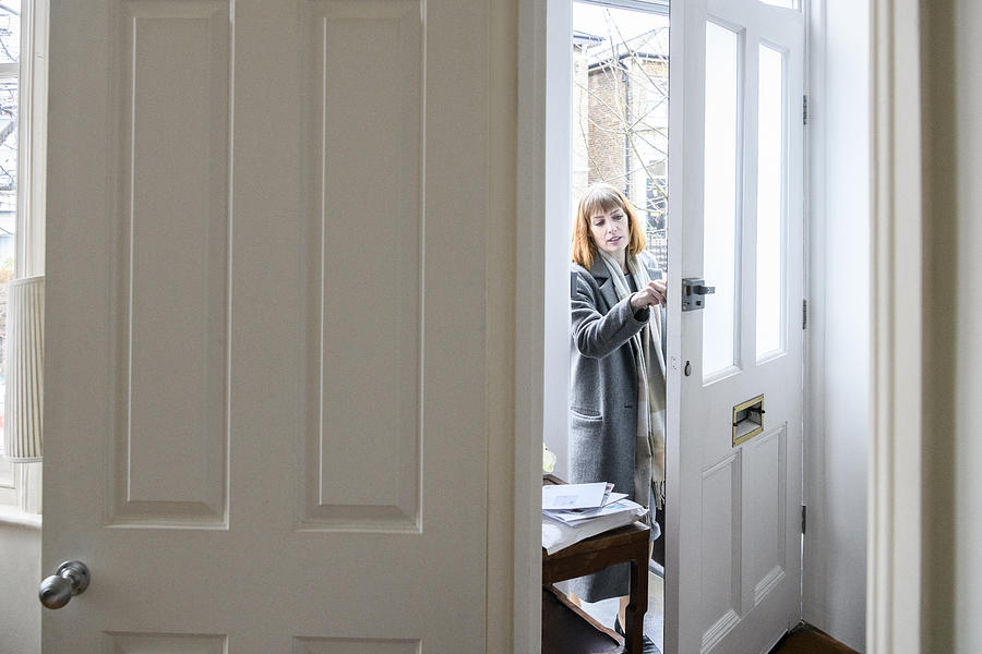 Mid adult woman unlocking front door and arriving home Photograph by JohnnyGreig