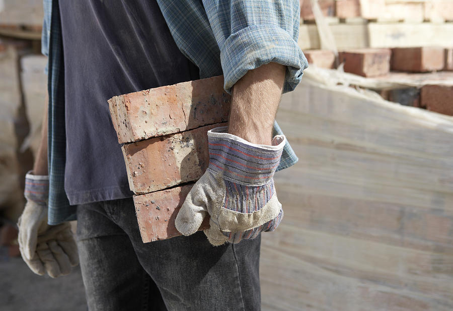 Mid Section of a Bricklayer Carrying Three Bricks With Protective Gloves Photograph by Digital Vision.