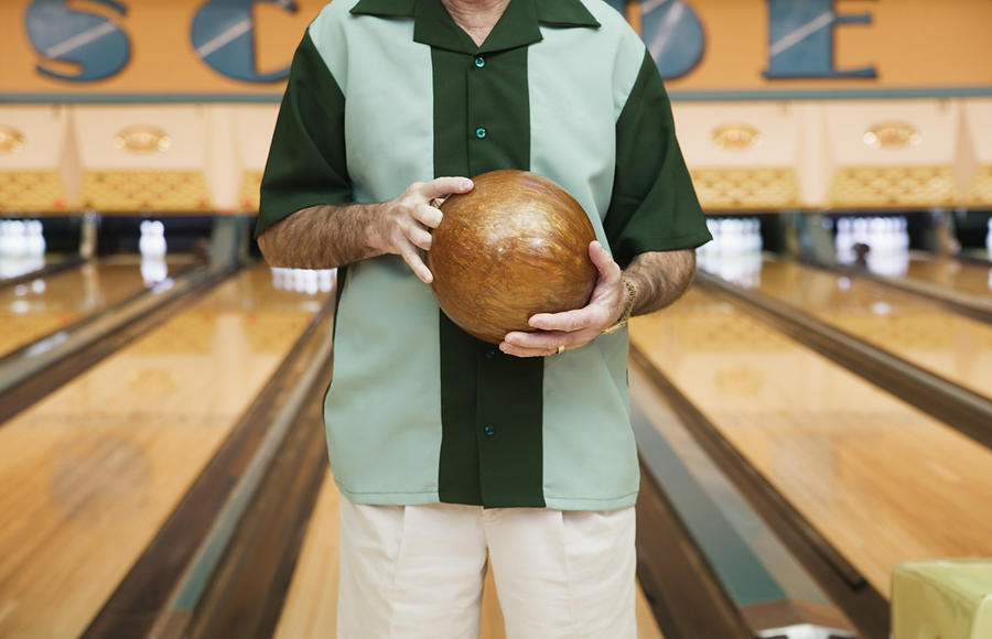 Mid section view of a mid adult man holding a bowling ball in a bowling alley Photograph by Colorblind Images LLC