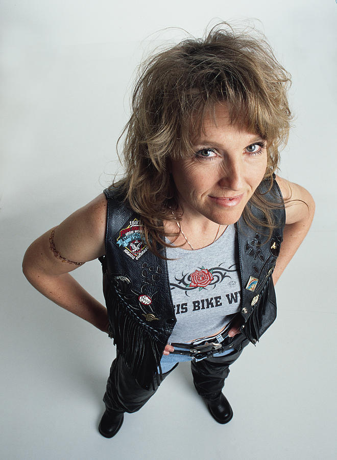 Middle Aged Adult Caucasian Female With Blonde Hair Wearing A Dark Leather Vest With Fringe And A Gray Tank Top Has A Tatoo On Her Right Arm And Looks Up At The Camera Smiling Mischievously Photograph by Photodisc