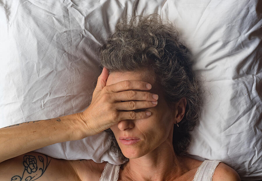 Middle aged woman with hand over eyes on pillow from abvove Photograph by Natalie_board