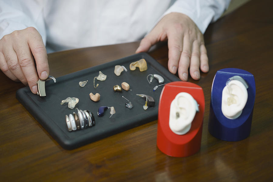 Midsection of audiologist various hearing aids at table in doctors office Photograph by Halfdark