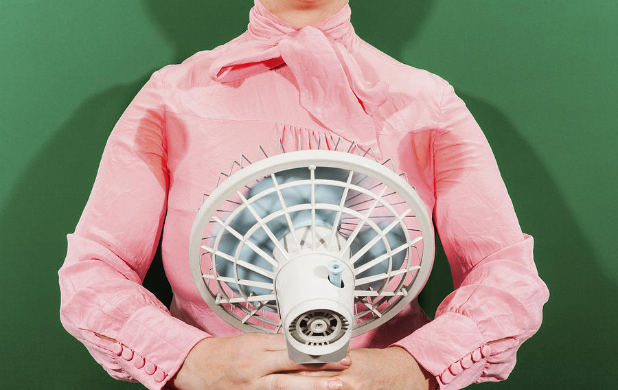 Midsection of businesswoman with sweaty armpits holding fan against green background Photograph by Paula Winkler