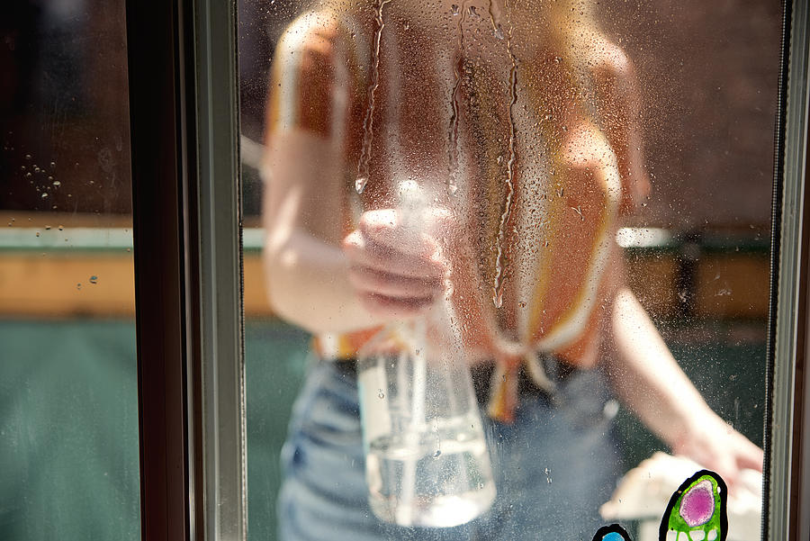 Millenial woman cleaning window on city balcony in spring. Photograph by Martinedoucet