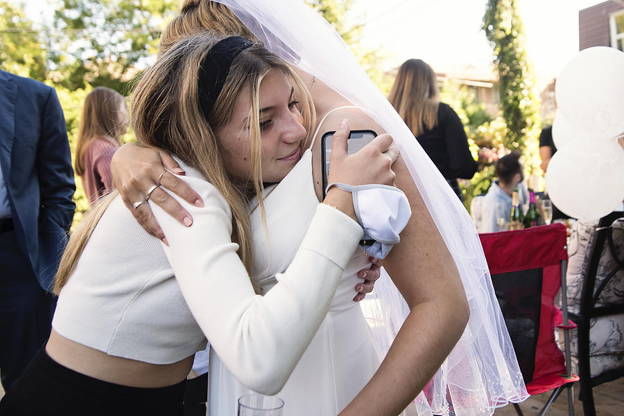 Millennial bride hugging cousin at wedding cocktail in backyard. Photograph by Martinedoucet
