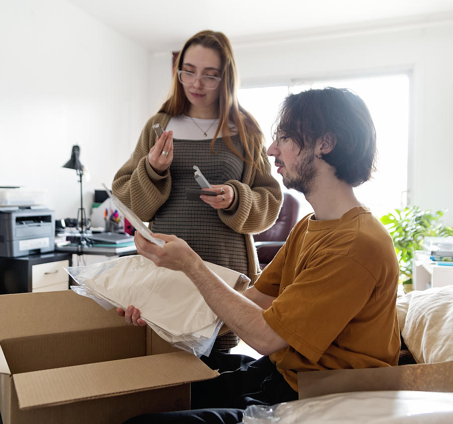 Millennial couple opening a delivered package in living room. Photograph by Martinedoucet