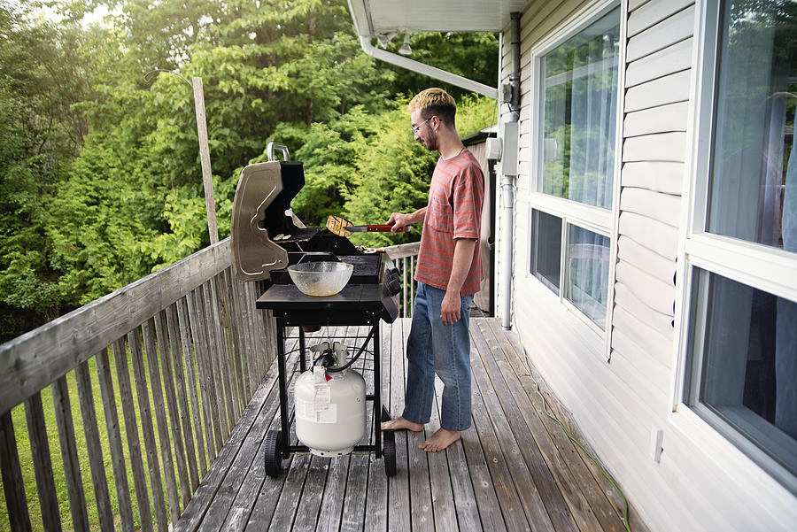 Millennial man cooking vegetables on barbecue in country house. Photograph by Martinedoucet