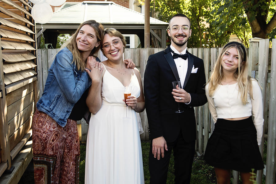 Millennial newlywed couple posing with family members in backyard. Photograph by Martinedoucet