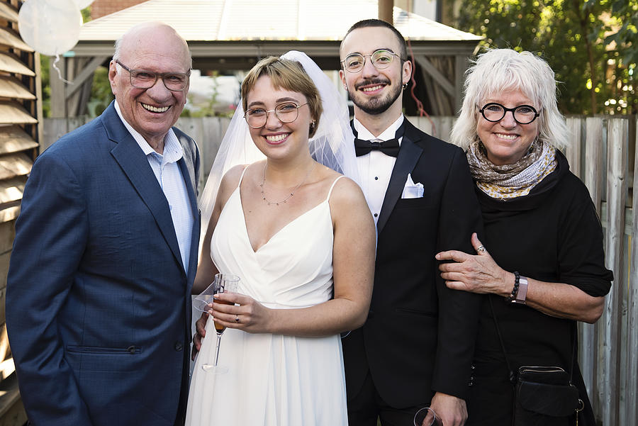 Millennial newlywed couple posing with grandparents in backyard. Photograph by Martinedoucet