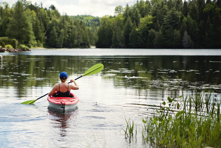 Millennial woman kayaking on country lake. Photograph by Martinedoucet