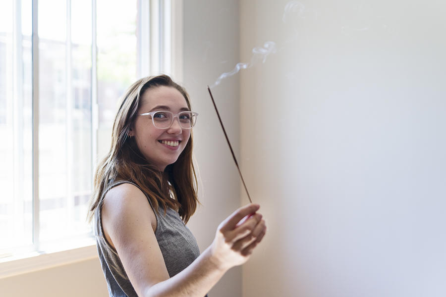 Millennial young woman purifying new apartment with incense. Photograph by Martinedoucet