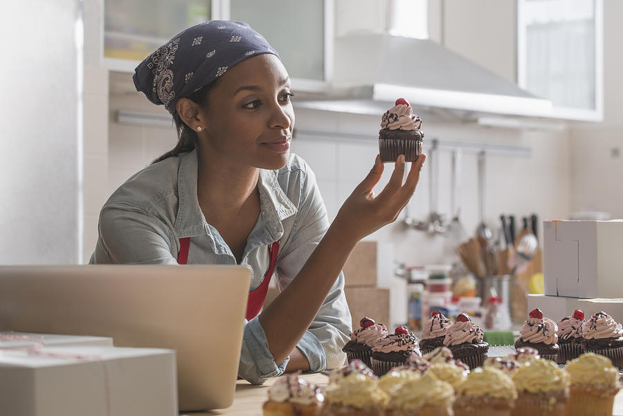 Mixed race baker admiring cupcake in commercial kitchen Photograph by Jose Luis Pelaez Inc