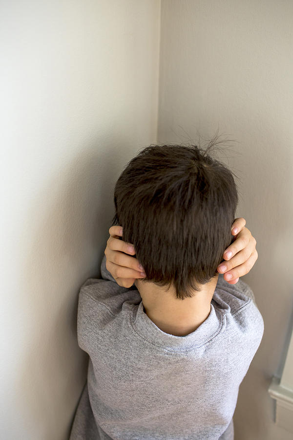 Mixed Race boy standing in corner covering ears Photograph by Adam Hester
