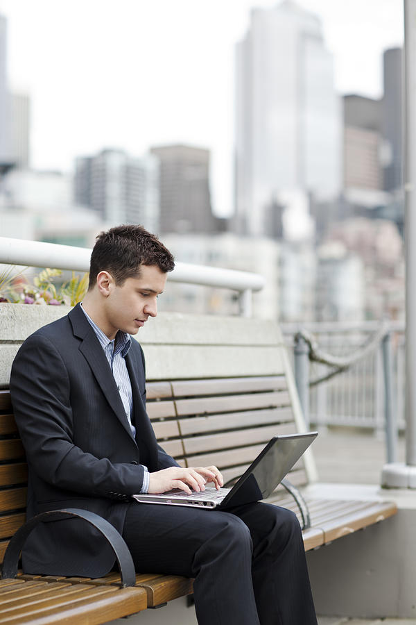 Mixed race businessman using laptop on city bench Photograph by Take A Pix Media