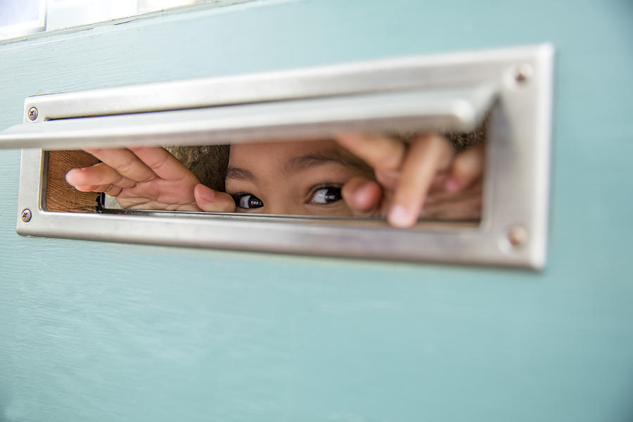 Mixed race girl peeking through mail slot Photograph by Inti St Clair