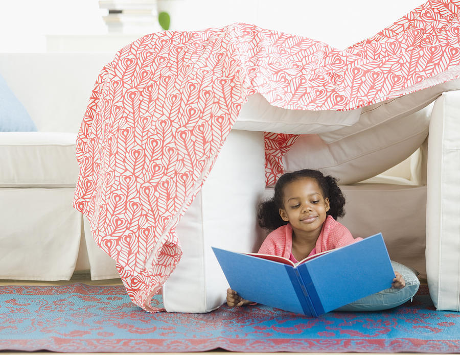 Mixed race girl reading in living room fort Photograph by Blend Images - JGI/Jamie Grill
