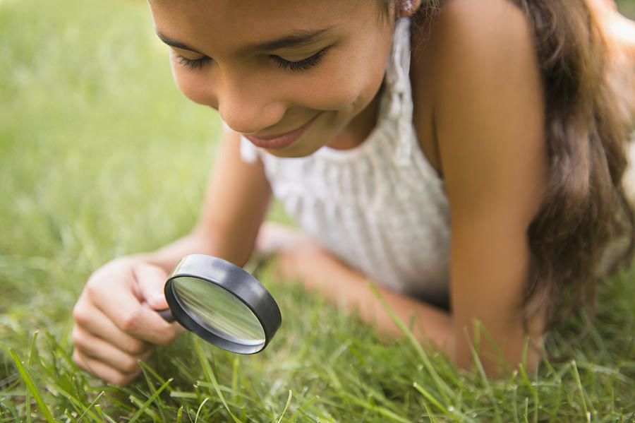 Mixed race girl using magnifying glass in grass Photograph by JGI/Jamie Grill