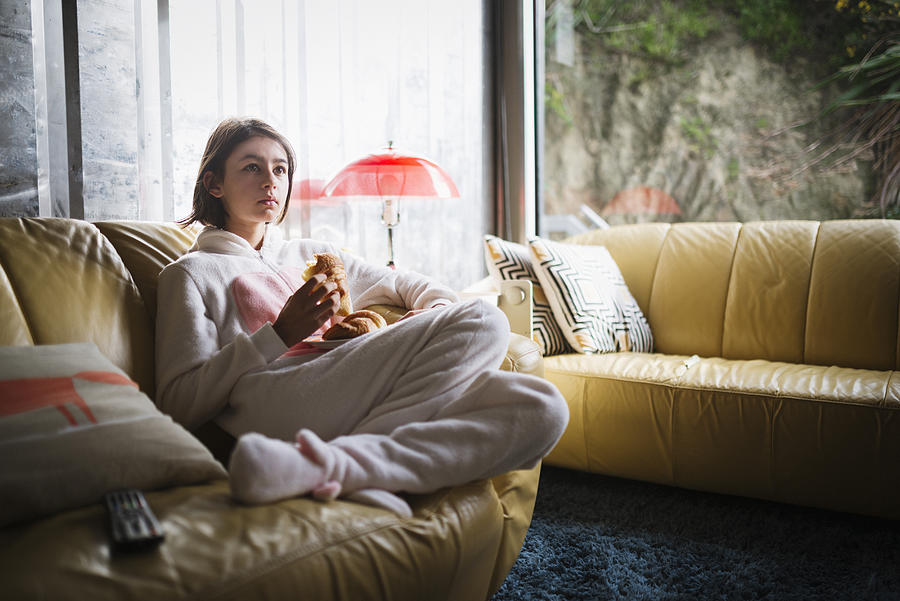 Mixed Race girl wearing rabbit costume sitting on sofa eating croissant Photograph by Donald Iain Smith