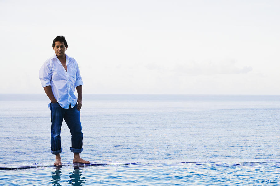 Mixed race man standing on edge of infinity pool Photograph by Jack Hollingsworth