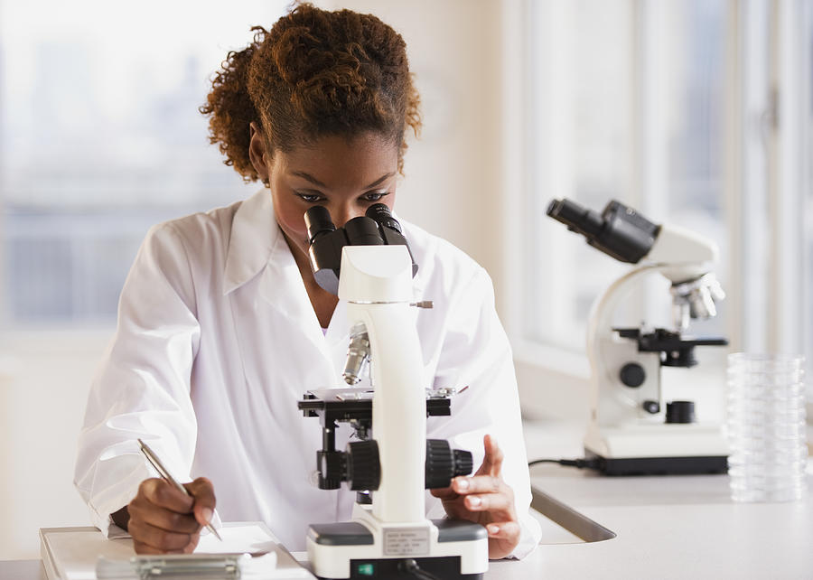 Mixed race scientist peering into microscope Photograph by JGI/Daniel Grill