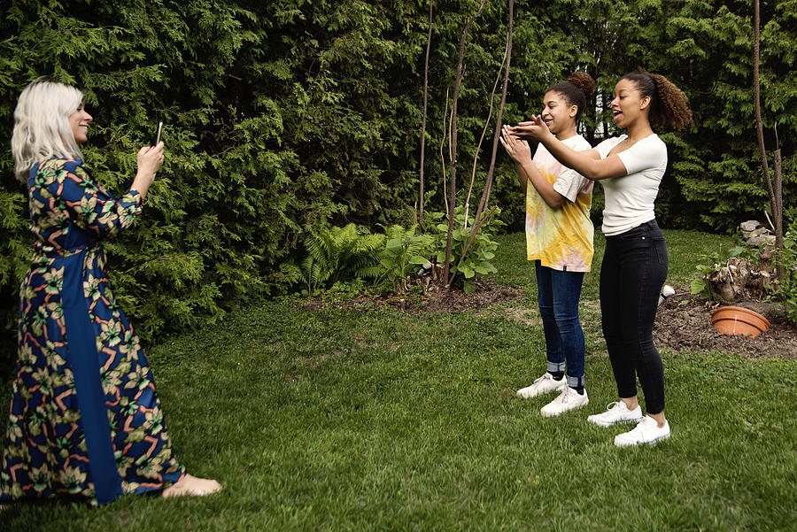 Mixed-race sisters being filmed by mother in backyard. Photograph by Martinedoucet