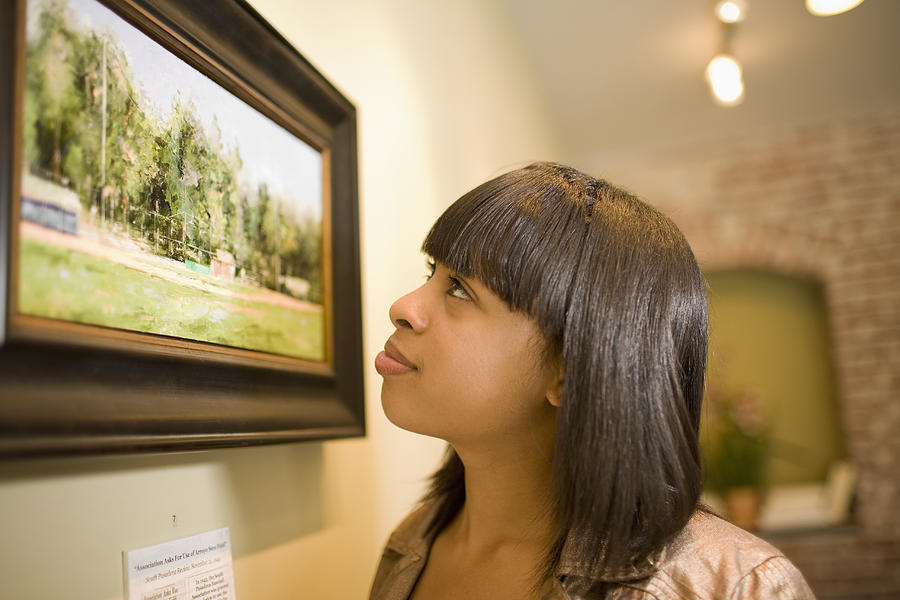 Mixed race woman admiring painting in gallery Photograph by Chicasso