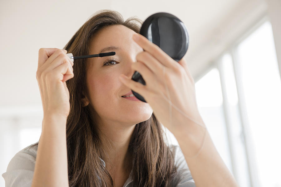 Mixed race woman applying makeup in compact mirror Photograph by JGI/Jamie Grill