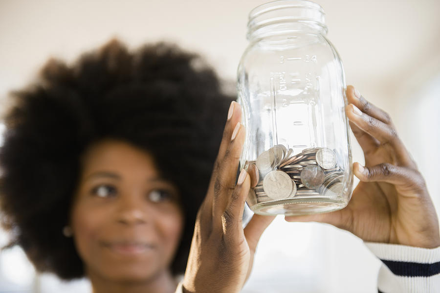 Mixed race woman holding jar of change Photograph by JGI/Jamie Grill