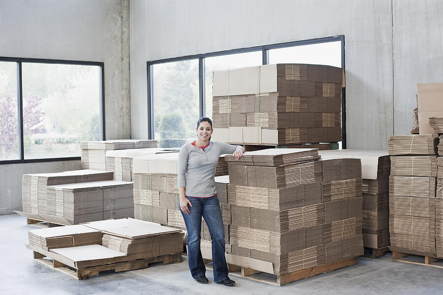 Mixed race woman leaning on flattened boxes in warehouse Photograph by Jetta Productions Inc