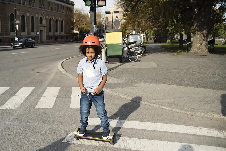 Mixed-race young boy on electric skateboard crossing street. Photograph by Martinedoucet