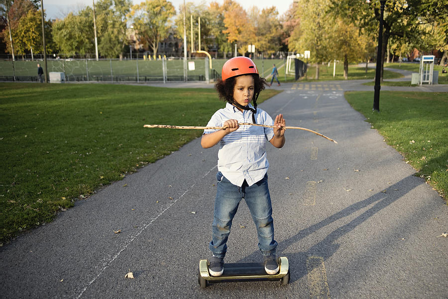 Mixed-race young boy on electric skateboard in urban park. Photograph by Martinedoucet