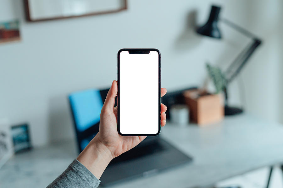 Mockup image of woman holding smartphone with blank white screen at home Photograph by Oscar Wong