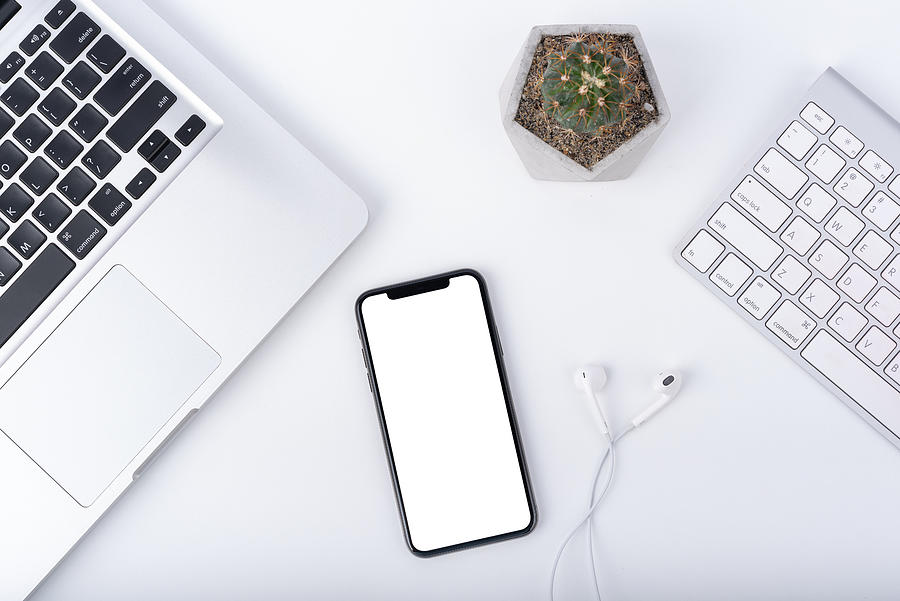 Modern white office work table with smartphone mock up laptop ,earphone and cactus, top view Photograph by Issarawat Tattong