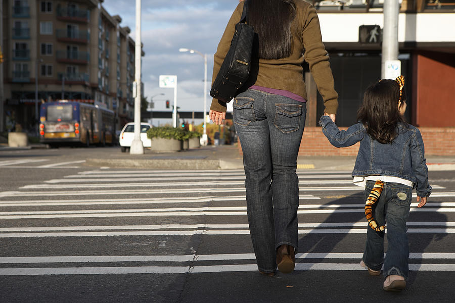 Mother and daughter (2-4) crossing street, holding hands, rear view Photograph by Thomas Northcut