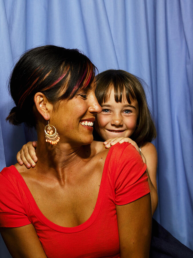 Mother and daughter (6-8) in photo booth, girl standing in background Photograph by Siri Stafford