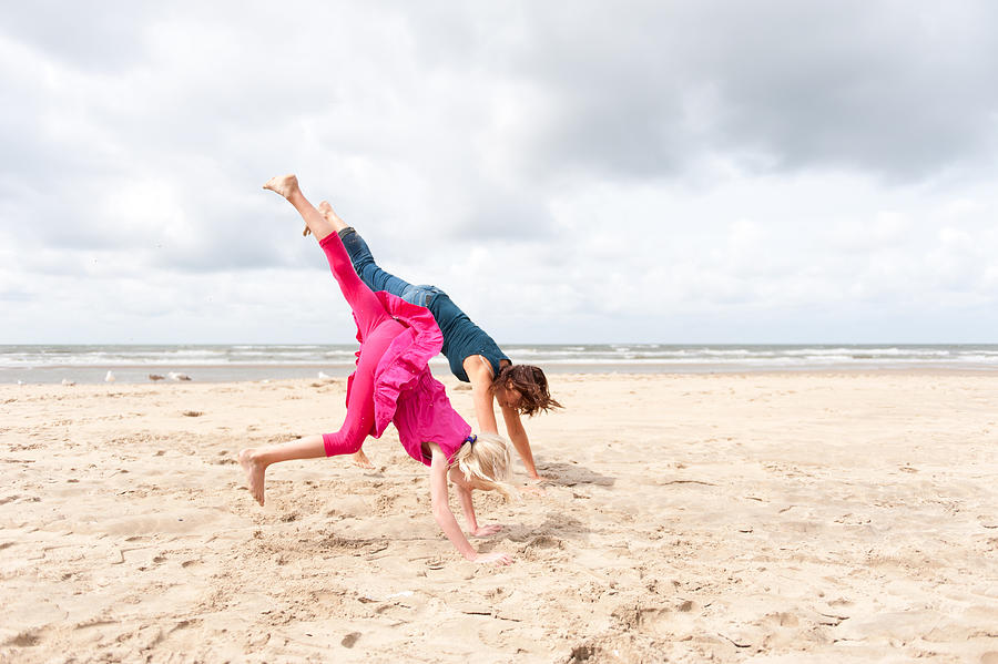 Mother and daughter doing handstand on the beach Photograph by Lucy Lambriex