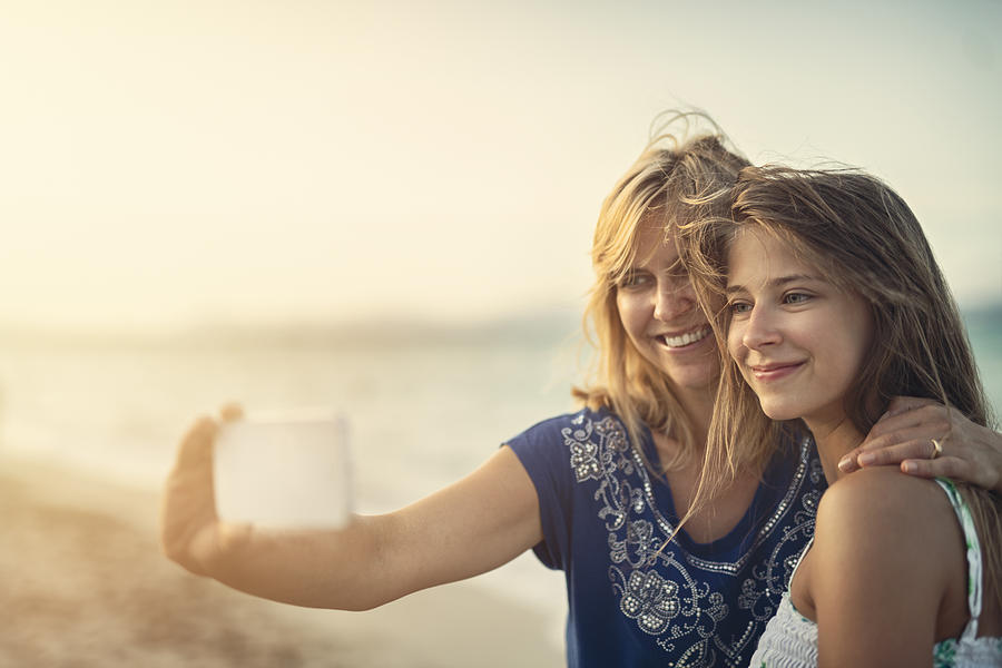 Mother and daughter embracing and taking selfies at the beach Photograph by Imgorthand