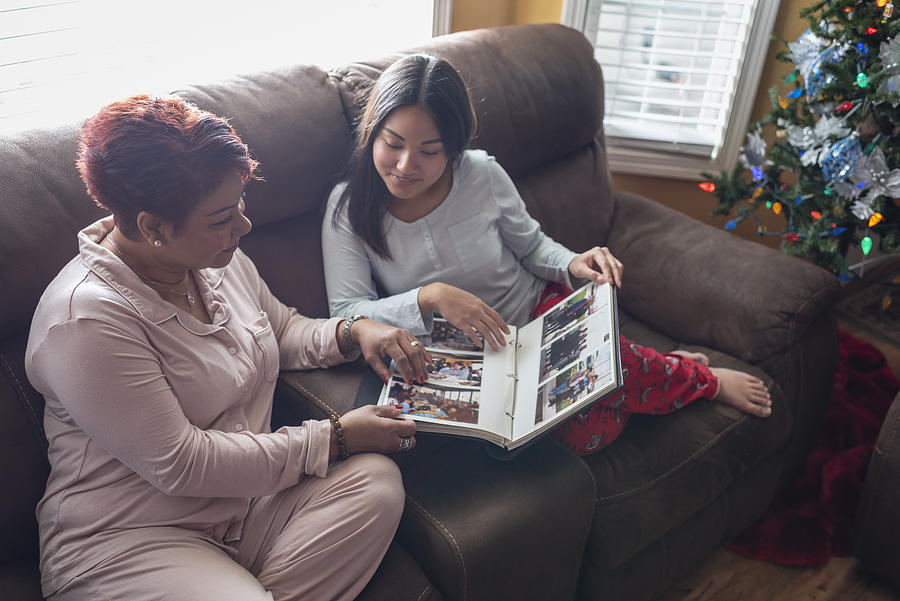 Mother and daughter looking at photo album near Christmas tree Photograph by Tony Anderson