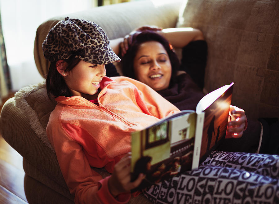 Mother and daughter reading book on sofa Photograph by Donald Iain Smith
