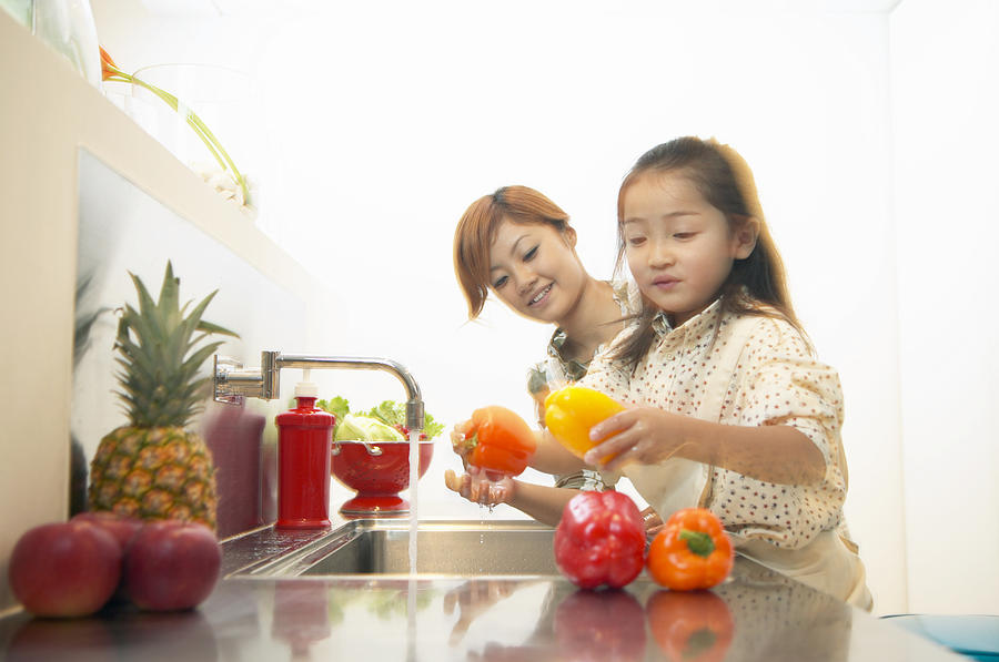 Mother and Daughter Washing Peppers at a Kitchen Sink Photograph by Digital Vision.