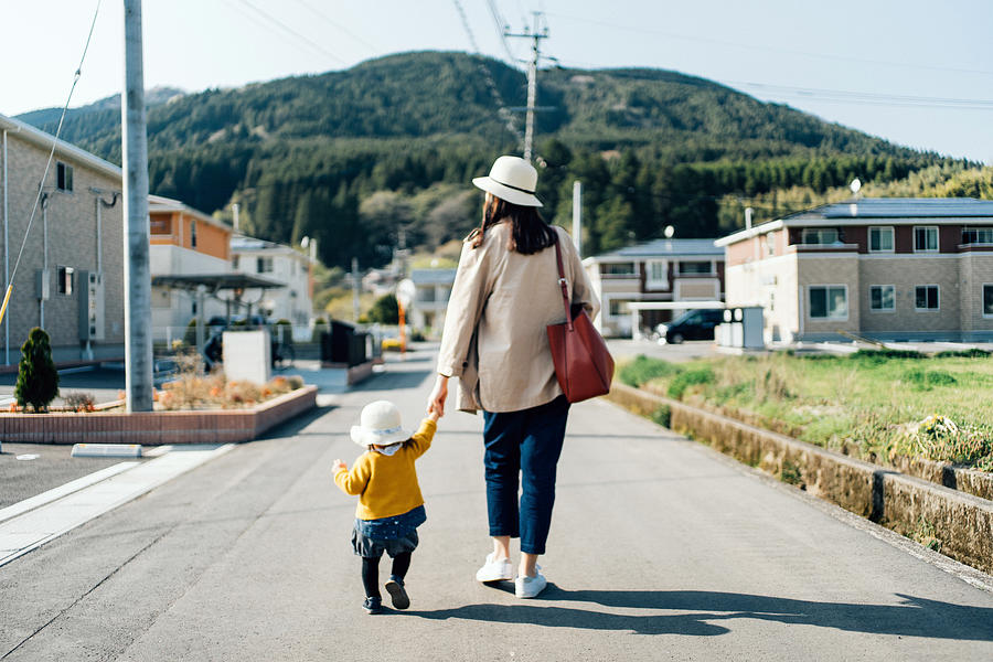 Mother and daughter with straw hat holding hands walking along town in the countryside on a sunny day Photograph by D3sign