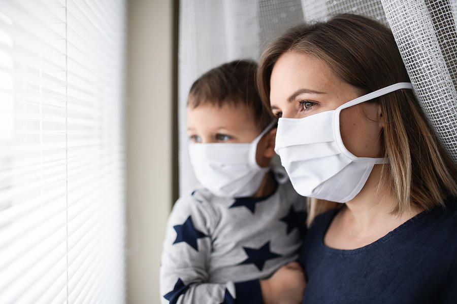 Mother and small son with face mask indoors at home, quarantine concept. Photograph by Halfpoint Images