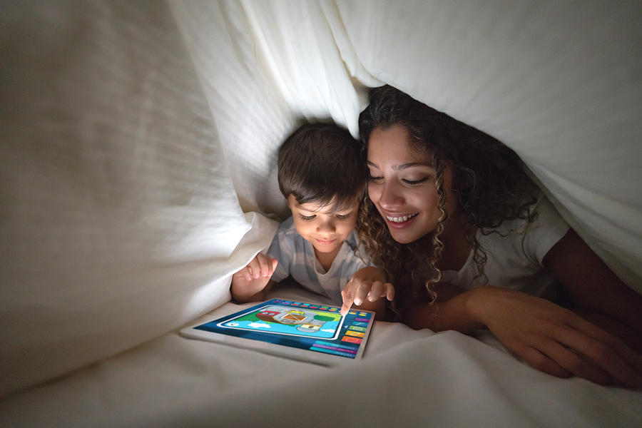 Mother and son playing on a digital tablet in bed Photograph by Andresr