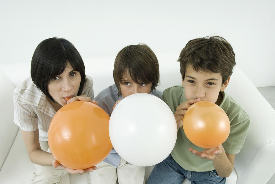 Mother and two sons inflating balloons, woman and one son looking at camera Photograph by PhotoAlto/Odilon Dimier