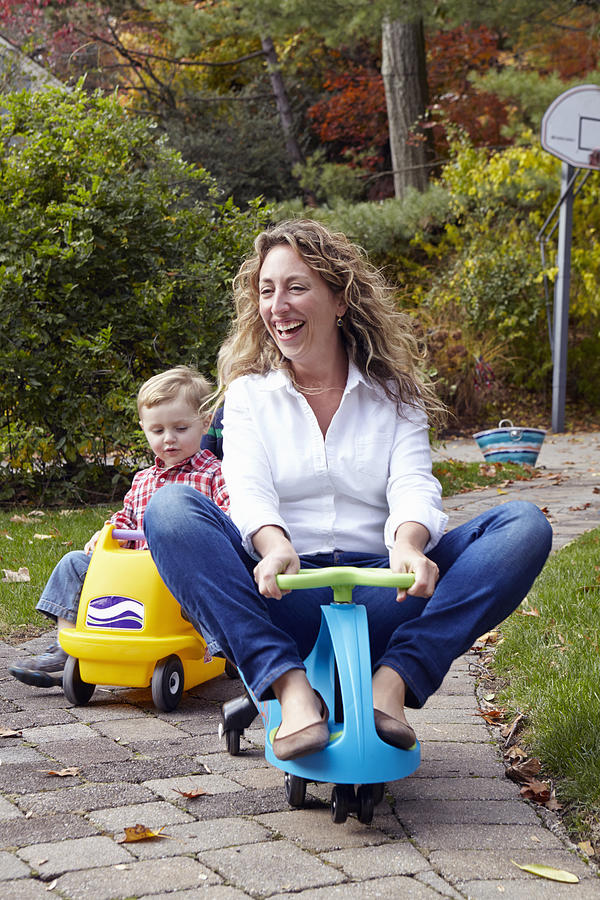 Mother and young son riding on toy cars in garden Photograph by Megan Maloy